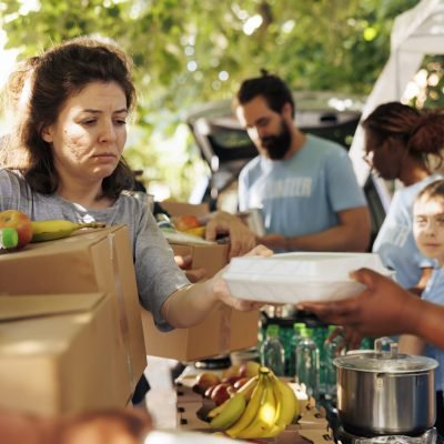 Diverse group provides aid, handing out meals to poor and needy individuals. Volunteers of all backgrounds come together to help the homeless, offering support through a charitable food drive.